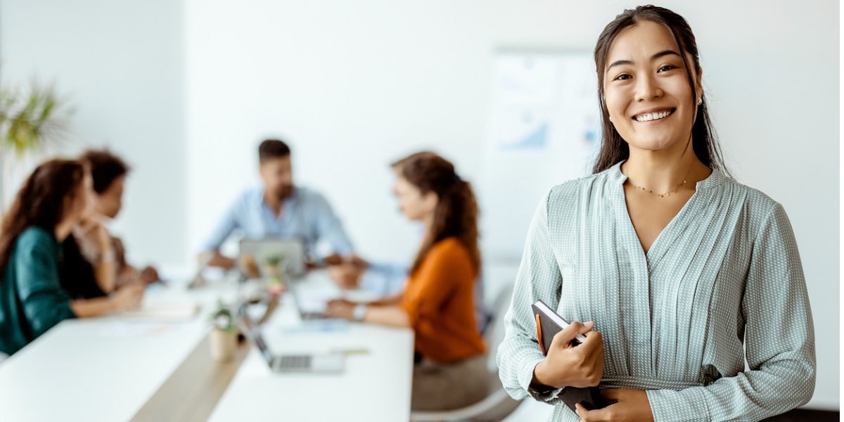 woman in the office smiling with meeting behind her