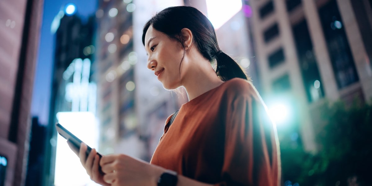 woman standing outside looking at phone in hand, city at night