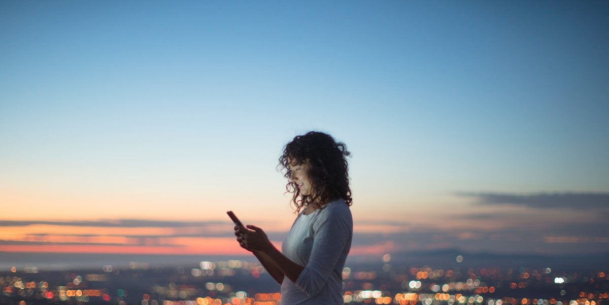 woman outside at dusk using cellphone, skyline in the background