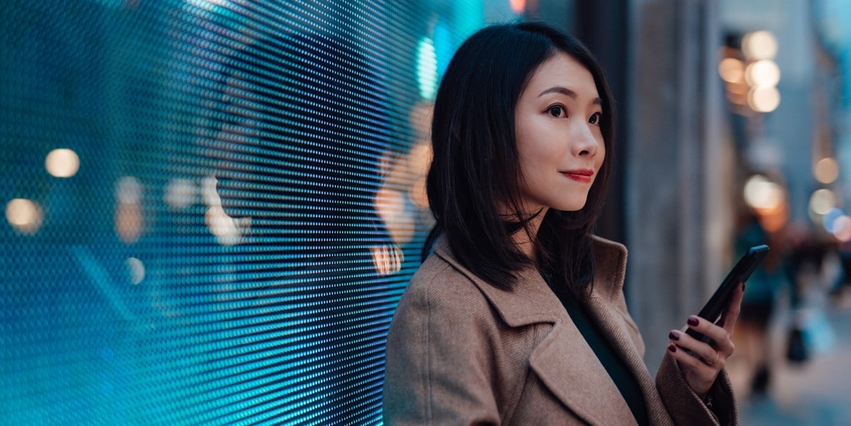 woman standing outside building, holding cellphone