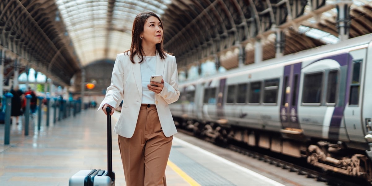 woman traveler holding cellphone and luggage, standing at train station platform