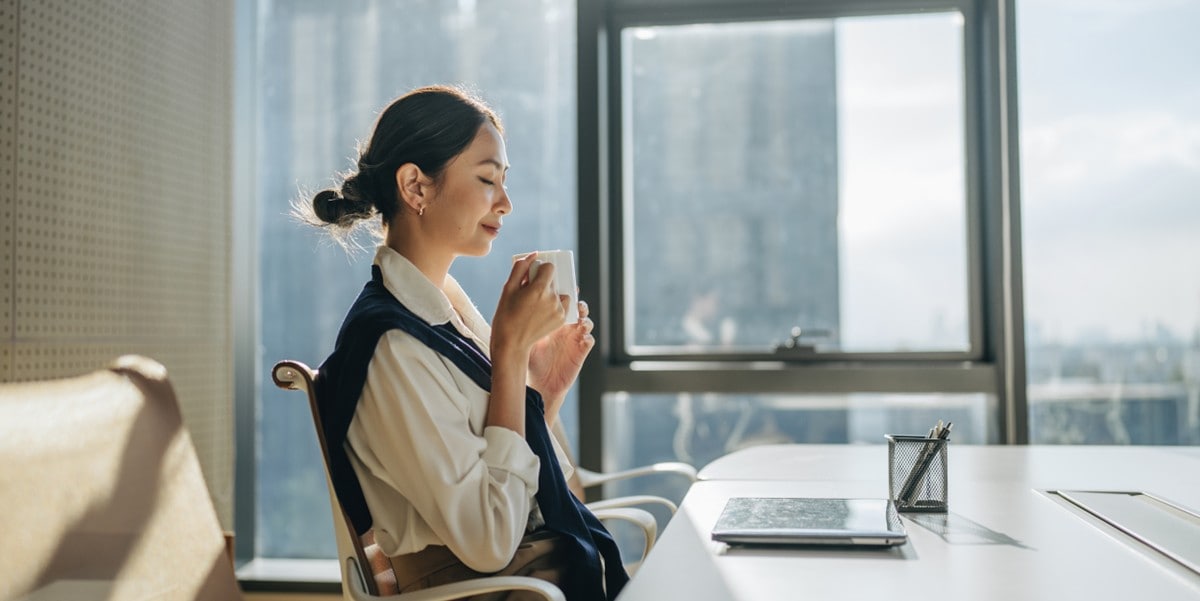professional woman seated at office desk holding a coffee cup