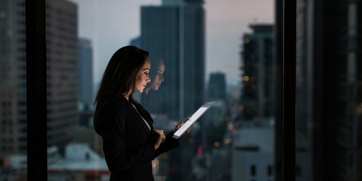 professional woman standing by window, looking at tablet