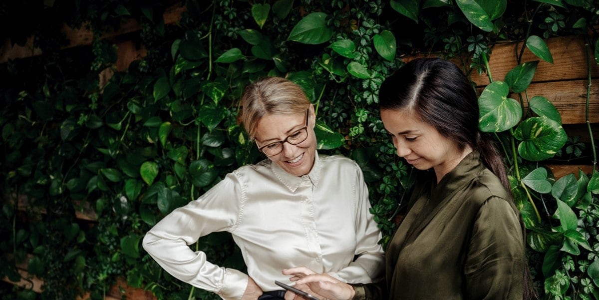 two professionals in front of greenery wall, looking at document