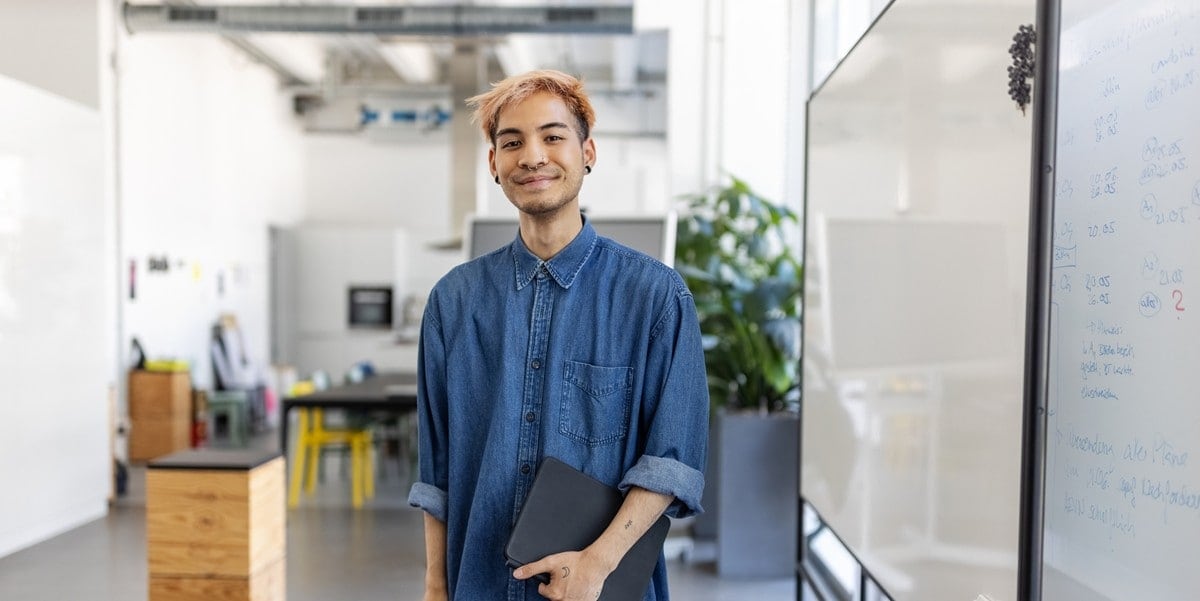 man in office smiling, holding a laptop