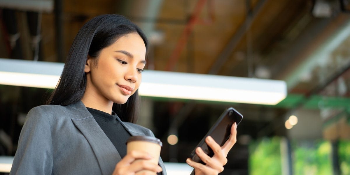 young professional in the office looking at phone in hand, coffee cup in hand