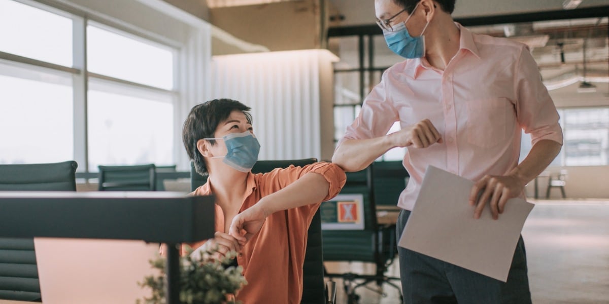 coworkers with masks giving each other an elbow bump