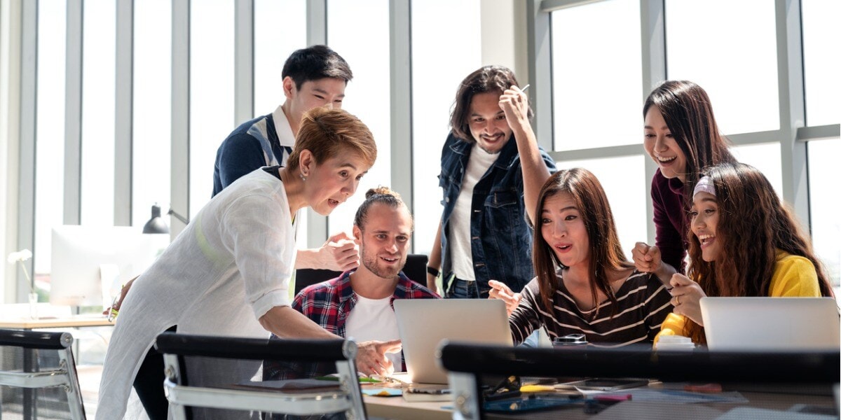 group of businesspeople gathered around one computer looking at the screen