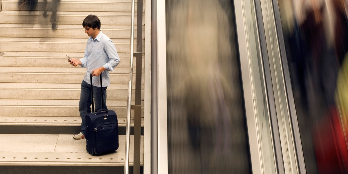 traveler standing on stairs with luggage, looking at cellphone