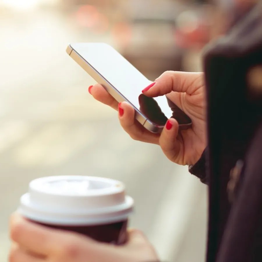 hands holding phone and coffee cup